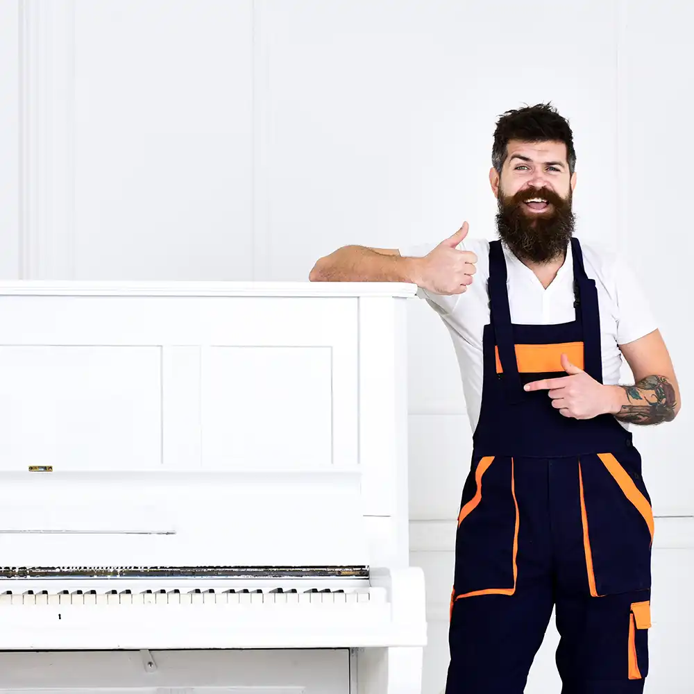 Mann mit Bart und Schnurrbart, Arbeiter in Latzhose lehnt sich an Klavier